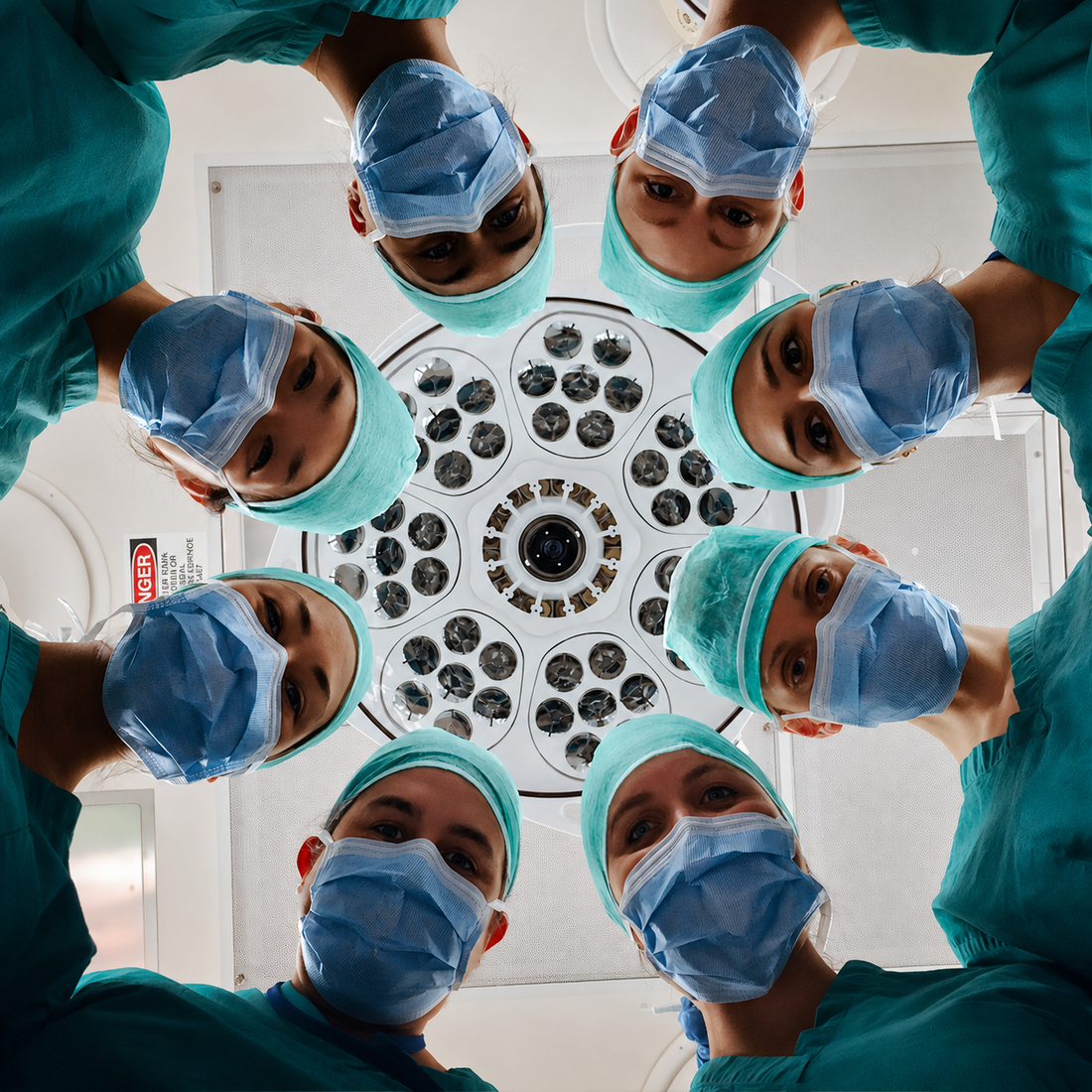 A sharp, color-restored operating room scene viewed from the patient’s perspective, showing a team of masked surgeons and medical staff leaning in a circle around the camera beneath a large surgical light.