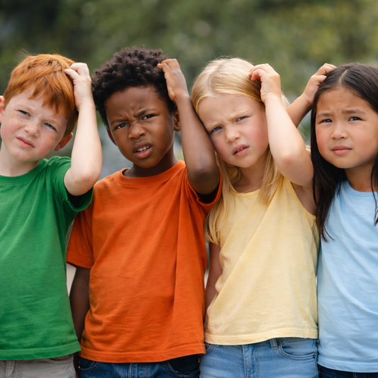Grupo de niños rascándose la cabeza con gesto de confusión, al aire libre, en una imagen cuadrada 1:1 con fondo desenfocado.